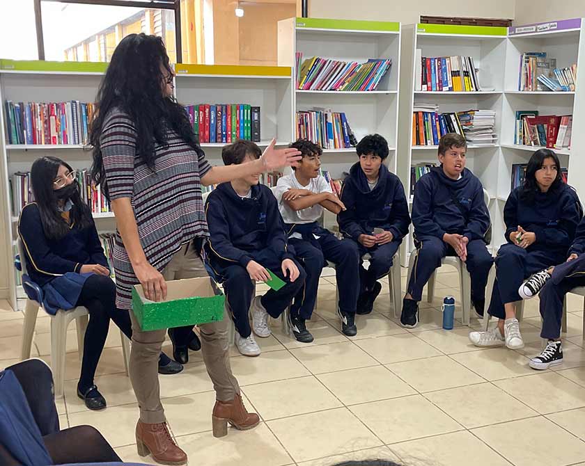Facilitadora de Global Shield guía una actividad de autoprotección con estudiantes sentados en círculo en la biblioteca del colegio